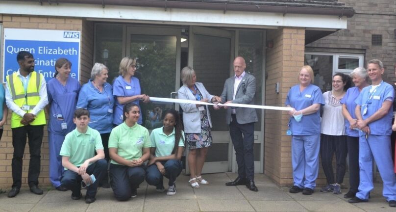 David Melia and Suzannah Cookson at a ribbon cutting event at Queen Elizabeth Vaccination Centre with other NHS staff.