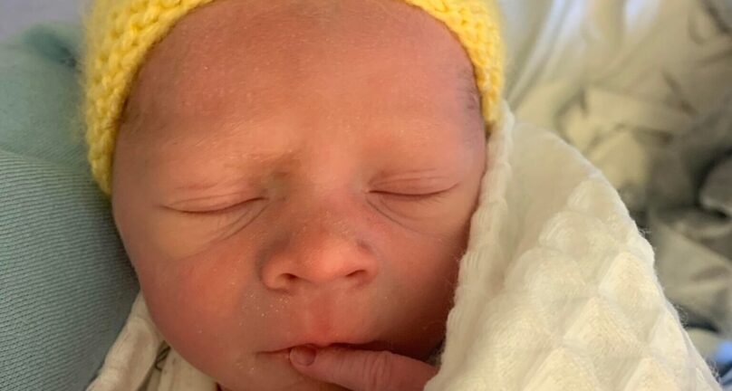 Image of newborn baby in hospital wearing a yellow knitted hat