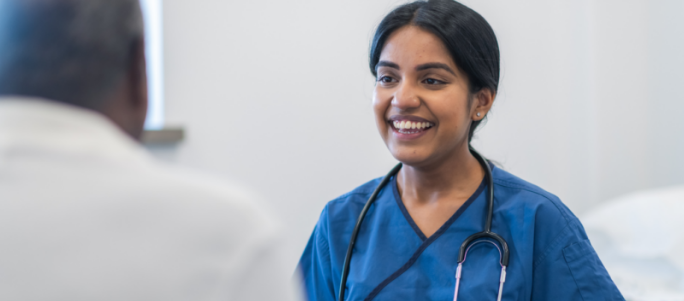 A female GP with stethoscope smiling at a patient whose back is to the camera