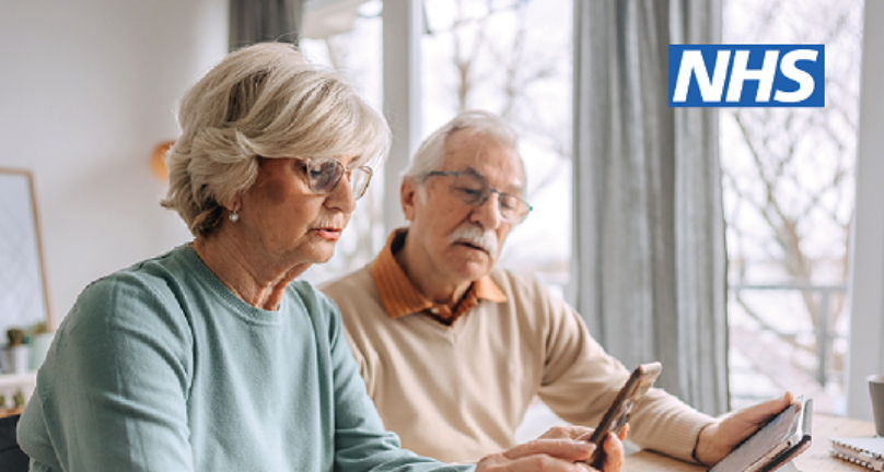An elderly couple sat at a table. One is using a mobile phone the other is also looking at whilst holding a tablet. Text in image reads; Eligible people can book their spring COVID-19 vaccine online or via the NHS App.