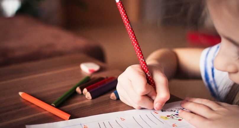 Child writing on paper with a pencil.