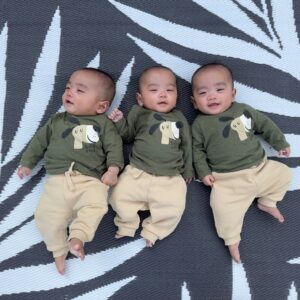 A photograph of baby boy triplets in matching outfits lying together on a blanket.