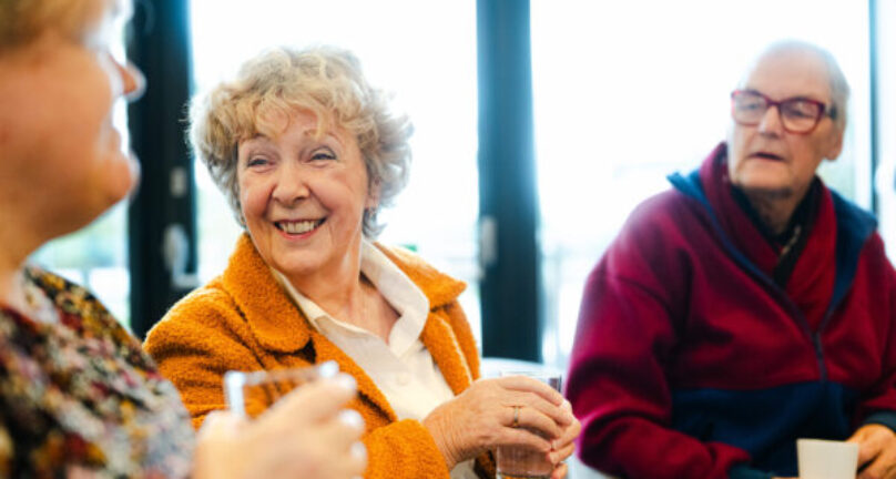 Group of friends chatting and smiling with hot drinks in cafe.