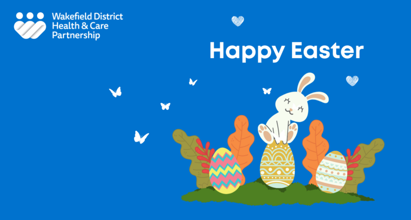 Happy Easter message on a blue background with a smiling white bunny sitting on decorated Easter eggs, surrounded by leaves and butterflies, with the Wakefield District Health and Care Partnership logo
